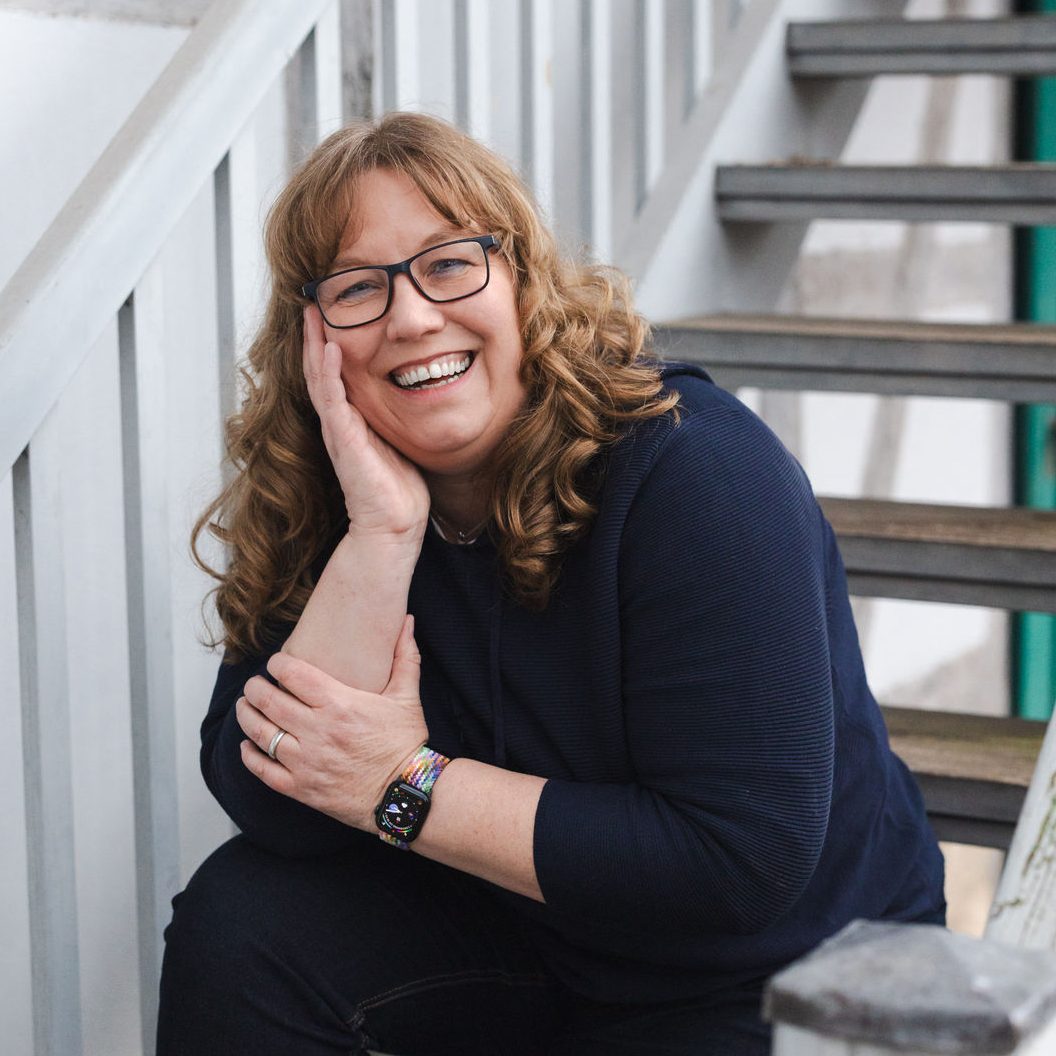 Petra Keck sitzt auf eine Hand gestützt auf einer Treppe und lacht in die Kamera.
